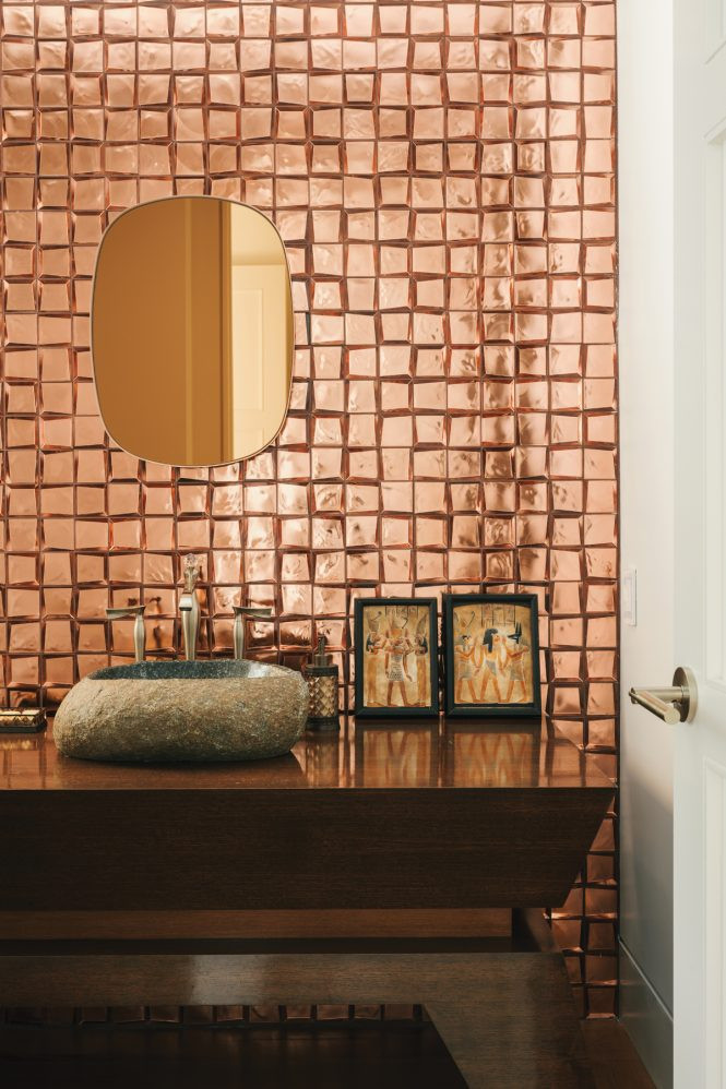 Irregularly shaped copper-backed tiles shimmer behind a sink cut from sculpted stone.