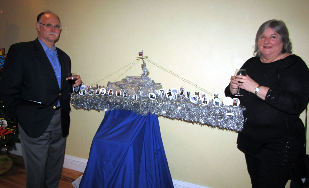 Phil Dore and Jill Dore, senior program manager of the General Dynamics Mission Systems&nbsp;Frigate Team, pose in front of the Team&#39;s battleship "tree" featuring photos of employees who served in the US Military.&nbsp;